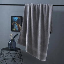 A gray premium pure cotton bath towel hanging on a rack next to a glass vase.