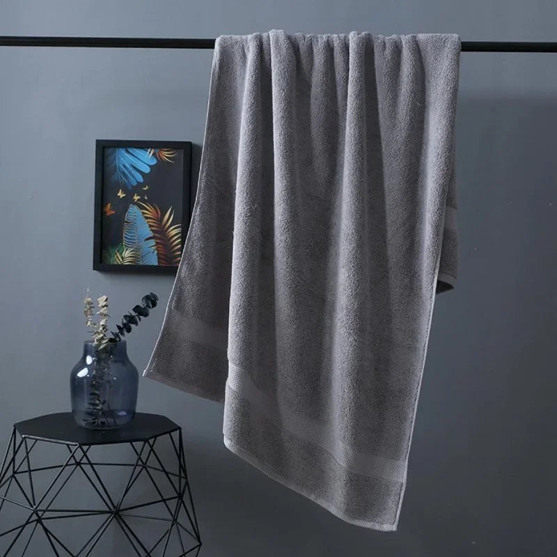 A gray premium pure cotton bath towel hanging on a rack next to a glass vase.
