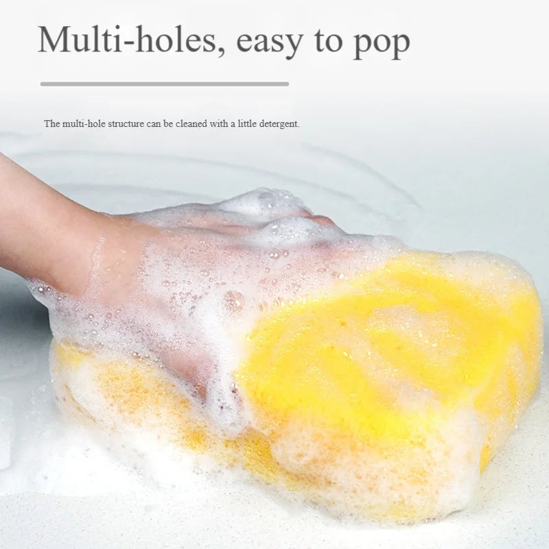 A hand is squeezing a yellow multi-hole sponge, covered in white soap suds.