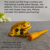 A handcrafted wooden frog percussion instrument with intentional crackle paint design resting on a gray surface.