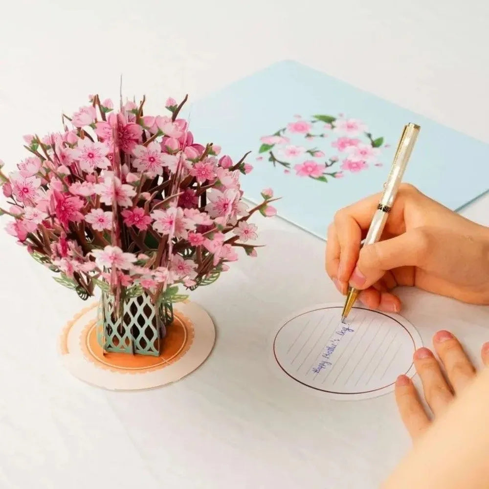 A hand is writing on a card next to a bouquet of pink cherry blossoms.