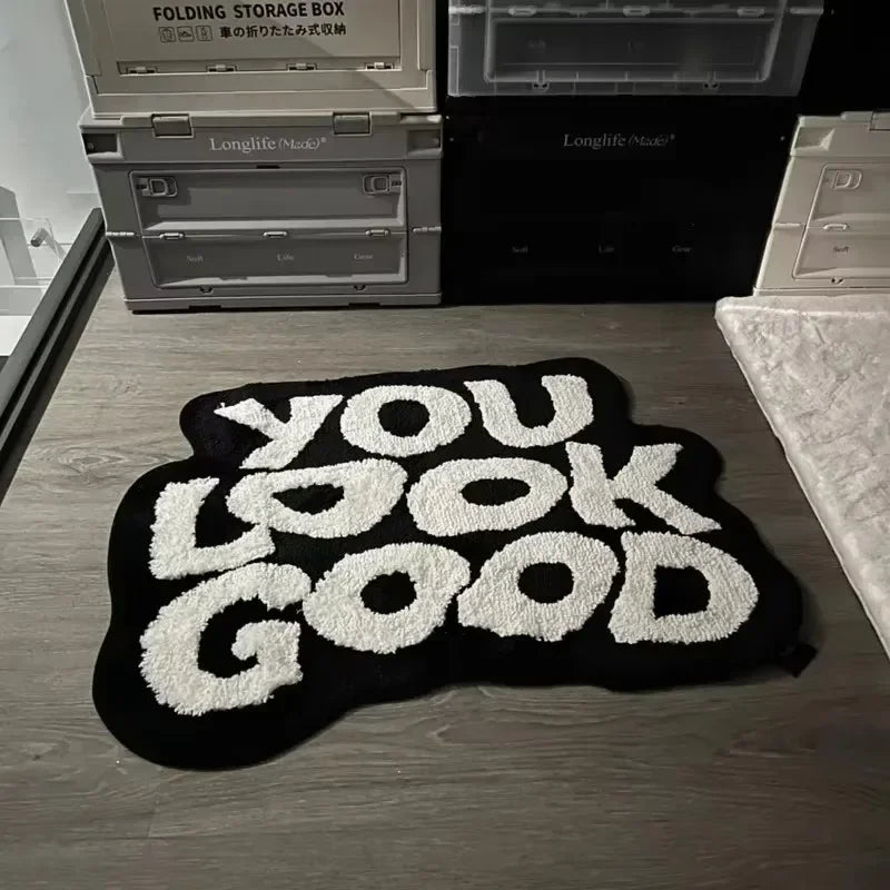 A black non-slip letter rug with white text that reads YOU LOOK GOOD is displayed on a wooden surface.