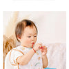 A baby is shown wearing a white and gold patterned waterproof full-body feeding bib with a sleeveless design.