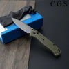 A folding knife with a drop point blade and olive green handle is shown resting on a blue box.