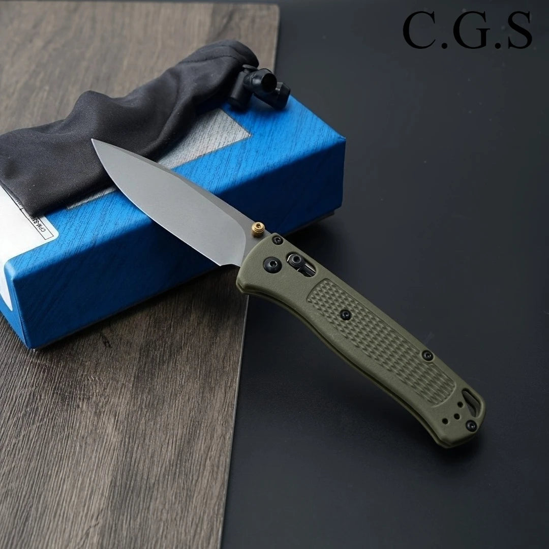 A folding knife with a drop point blade and olive green handle is shown resting on a blue box.