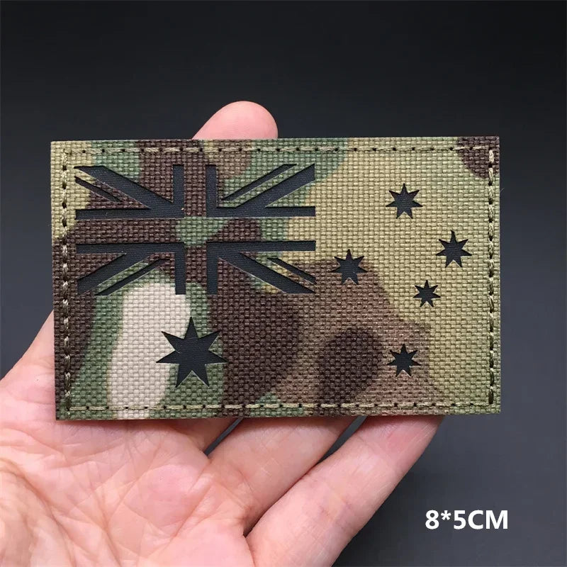 A dark green camouflage patch featuring a silhouette of the Union Jack flag and stars on a hand.