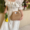 A woman wearing a white dress holds a woven straw chain crossbody handbag.