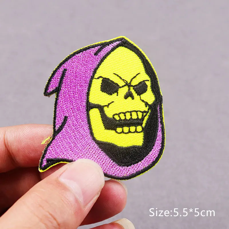 A purple embroidered patch featuring a yellow skull design being held by a hand.