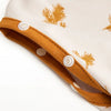 A close-up of a beige baby sleep sack with a mustard yellow trim and embroidered pine branch pattern.