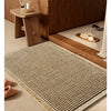 A rectangular beige waffle weave bath mat with tassels resting on a wooden shelf next to a dark wood cabinet.
