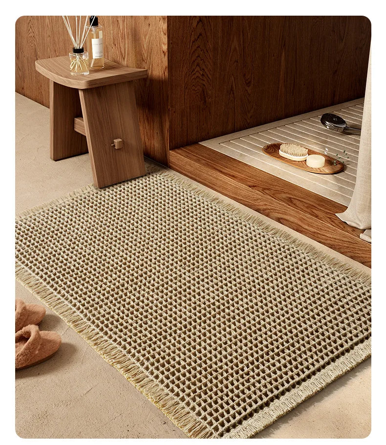 A rectangular beige waffle weave bath mat with tassels resting on a wooden shelf next to a dark wood cabinet.