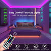 A hand holds an RGB LED strip light remote control in front of a bedroom setup with purple ambient lighting.