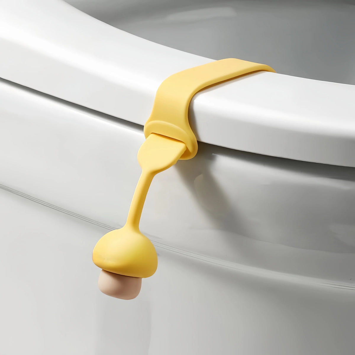 A yellow silicone toilet seat lifter with a pull ring is shown attached to a white toilet bowl.