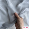 A hand is gently folding a piece of light gray, sheer silk chiffon fabric.