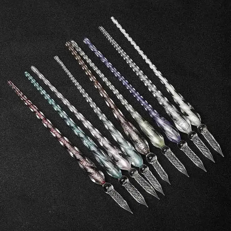 Colección de plumas de inmersión de cristal con tinta dorada, dispuestas en diagonal sobre una superficie oscura.