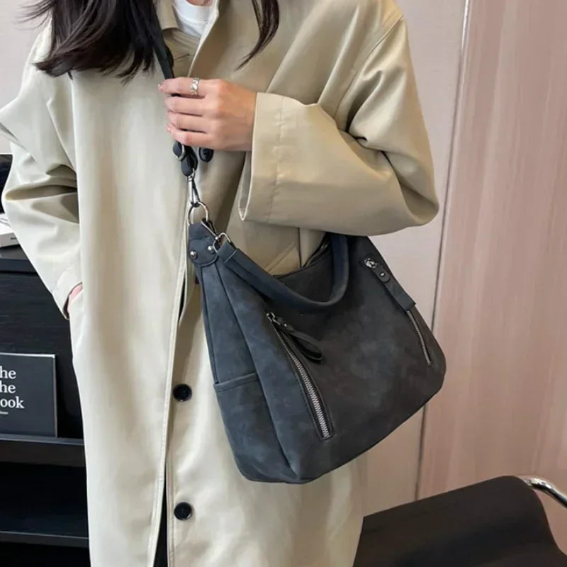 A beige trench coat is shown wearing a dark gray matte leather crossbody hobo bag.