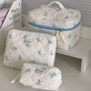 A white quilted cosmetic bag with a bow print and blue trim is displayed on a shelf.