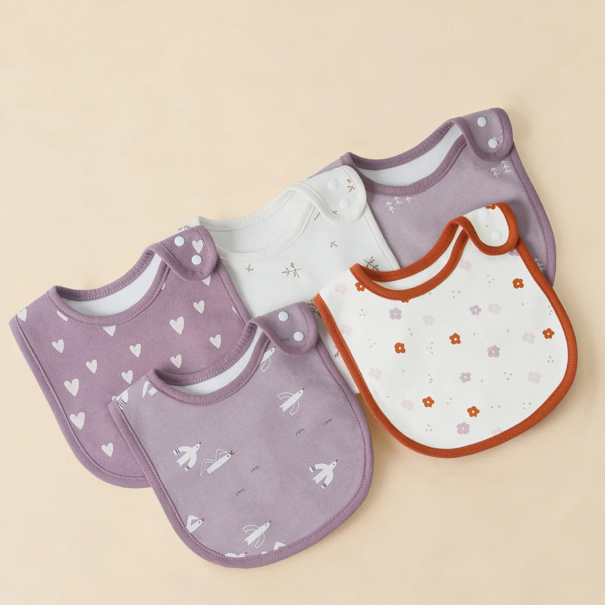 A set of purple and white cotton baby bibs with a U-shaped design are displayed on a light background.