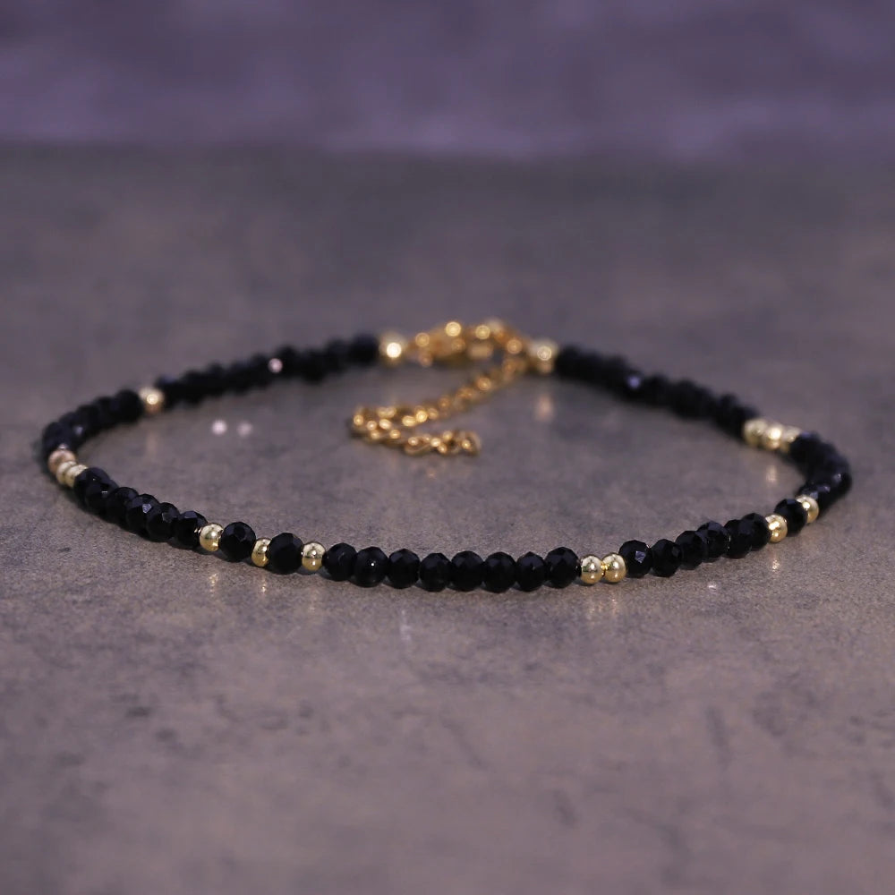 A black beaded bracelet with gold accents is displayed on a gray surface.