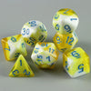 A set of seven polyhedral dice in yellow and white are arranged on a gray surface.