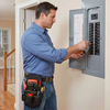 A man wearing a blue shirt and jeans is using an orange tool to operate a gray adjustable waist tool pouch on a door.