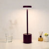 A dark purple LED desk lamp with a cylindrical base and a rectangular light shade illuminates a white surface.