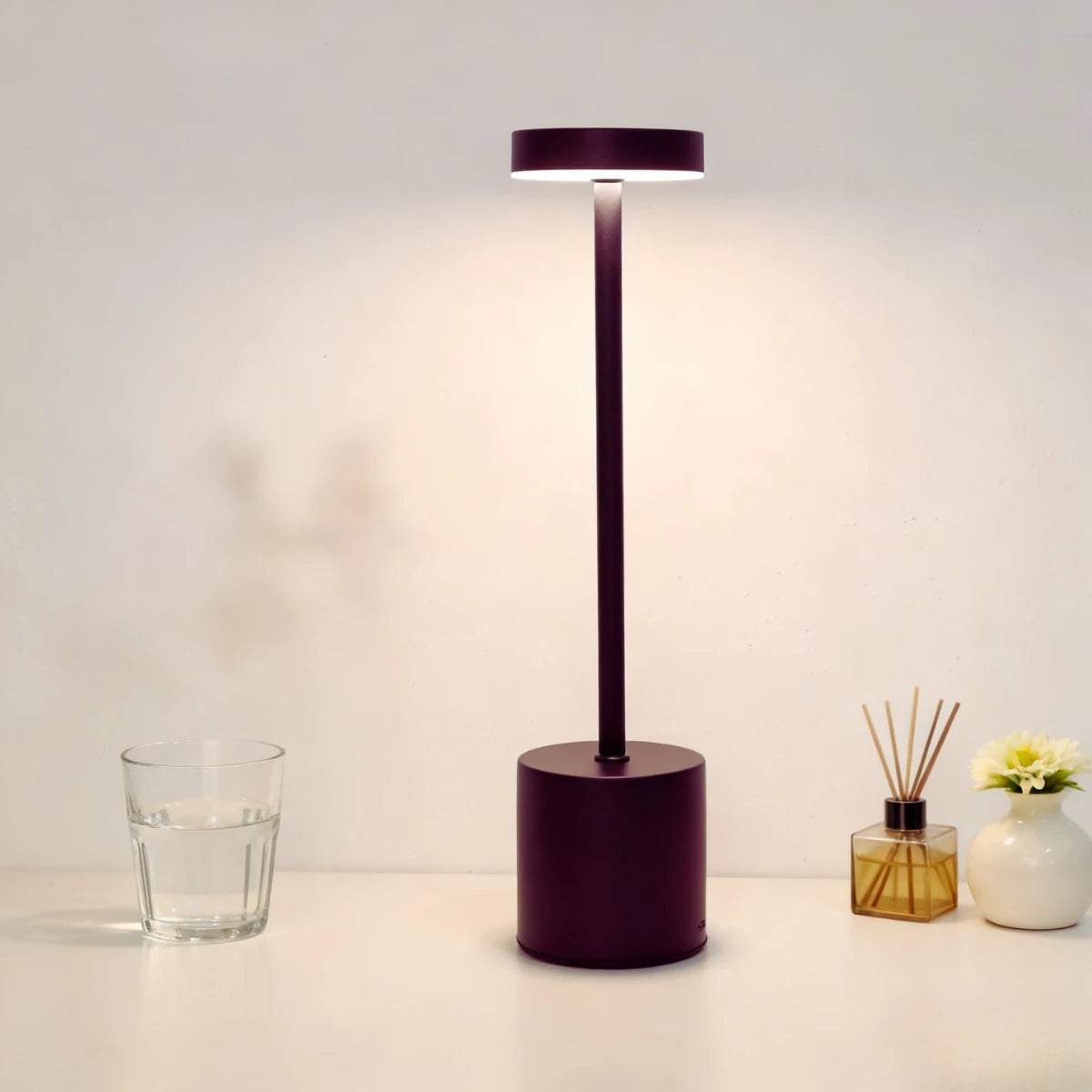 A dark purple LED desk lamp with a cylindrical base and a rectangular light shade illuminates a white surface.