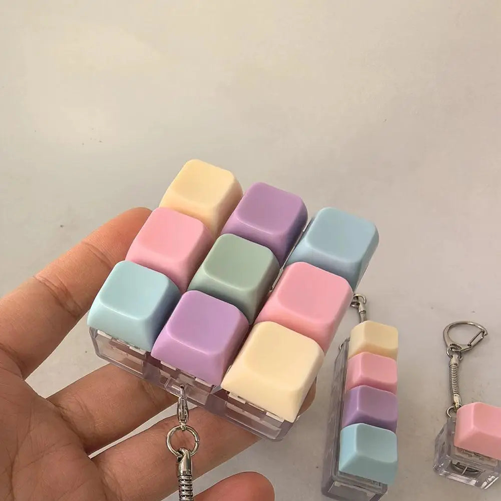 A hand holds a clear plastic keychain featuring multiple pastel colored mechanical keyboard fidget cubes.