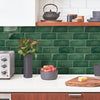 A kitchen backsplash featuring dark green subway tiles, a white countertop, and various cooking and food items.