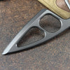 A compact stainless steel neck knife with a blade visible in its sheath, resting on a brown surface.