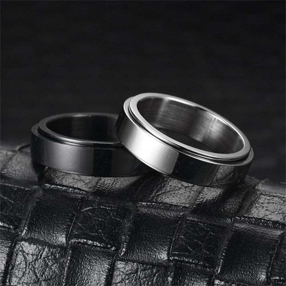 A close-up, black and white photo of a stainless steel anxiety spinner ring resting on a dark leather surface.