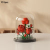 A clear glass dome display featuring a miniature arrangement of red roses and white filler flowers.