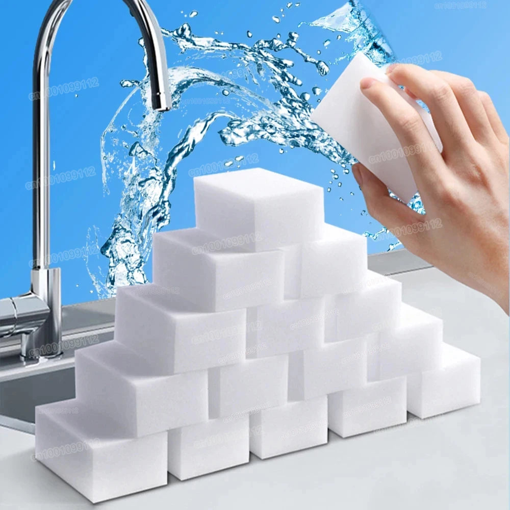 A hand is squeezing a white melamine cleaning sponge under running water, with a stack of similar sponges in the foreground.
