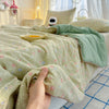 A hand is touching a light green floral quilt blanket on a bed, with a folded sage green throw draped over it.