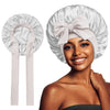 A woman models a light pink satin silk sleep bonnet tied in a bow, showing the fabric and style.