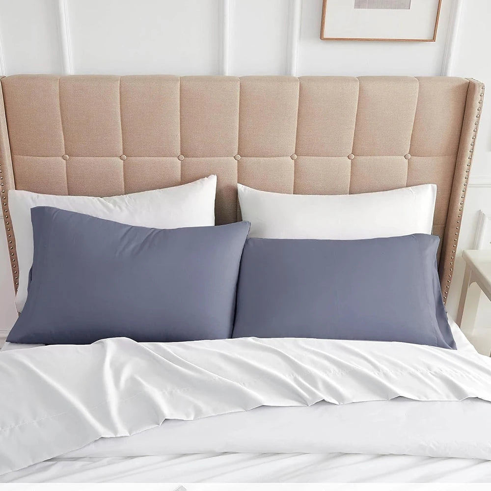 A set of two soft microfiber pillowcases in gray and white resting on a beige upholstered headboard.