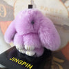 A fluffy lavender bunny keychain with a pom pom tail displayed on a dark surface.