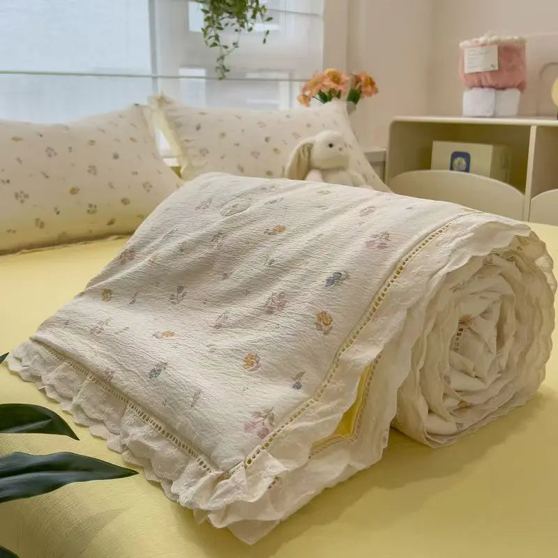 A rolled white floral washed cotton gauze summer quilt resting on a yellow surface.