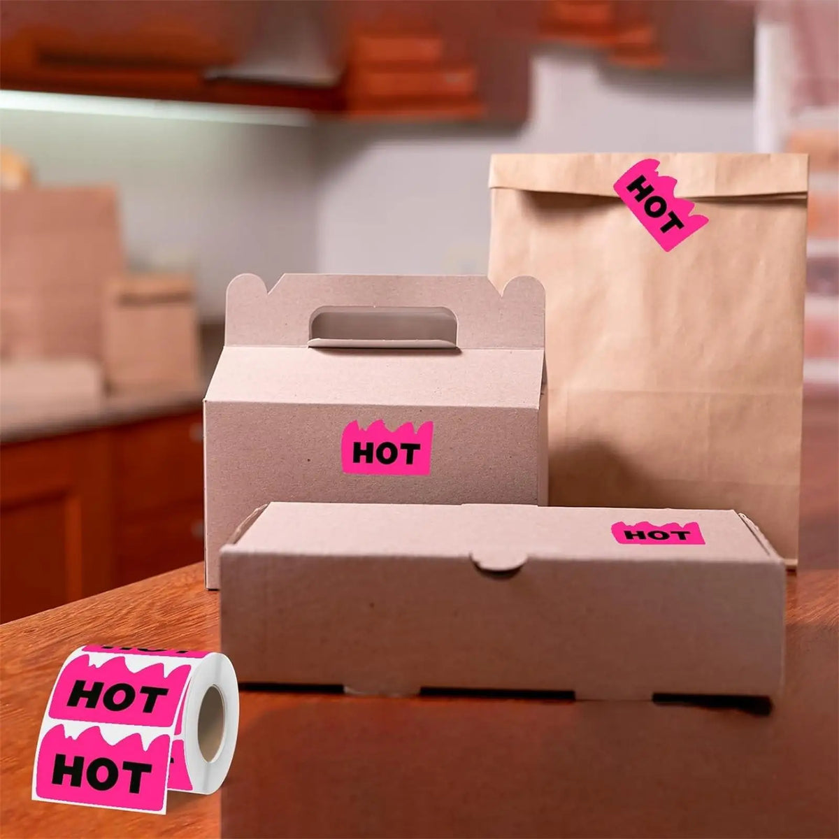 A cardboard box of pink stickers labeled HOT is shown next to a brown paper bag and a roll of pink stickers.
