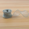 A roll of satin ribbon is unwinding, showing a wide strip of sheer, light beige fabric.