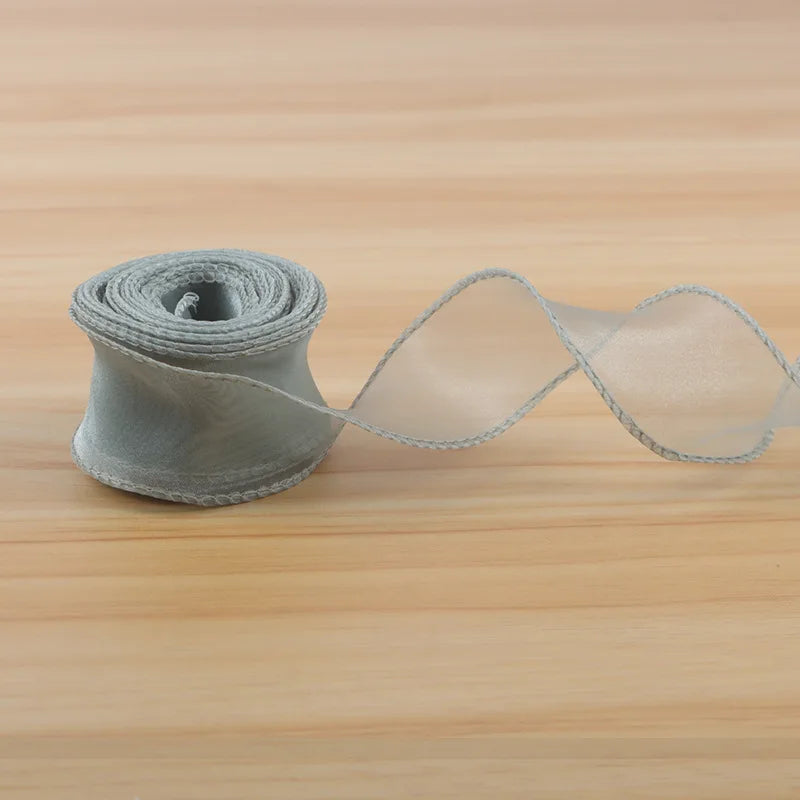 A roll of satin ribbon is unwinding, showing a wide strip of sheer, light beige fabric.