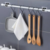 A silver curtain rod with hooks holding a silicone spatula and three wooden spatulas on a gray tiled wall.