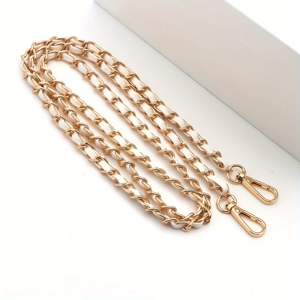 Gold-toned classic metal chain purse strap with a secure buckle laid on a white surface.
