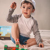 A young boy is holding a magnetic building block set on a white blanket with other blocks nearby.