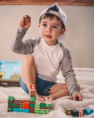 A young boy is holding a magnetic building block set on a white blanket with other blocks nearby.