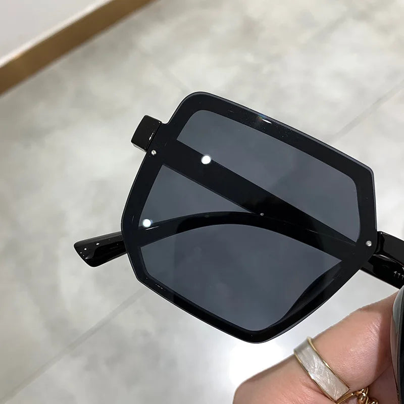 Primer plano de unas gafas de sol cuadradas vintage negras sostenidas por una mano.