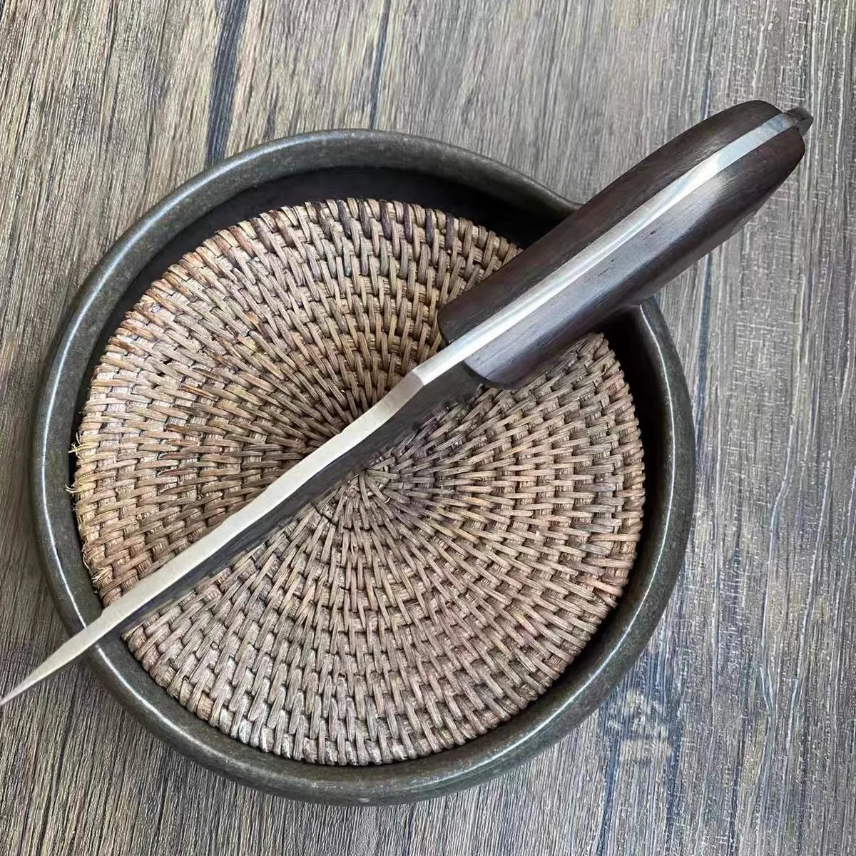 A handcrafted high-carbon stainless steel chef knife with a wooden sheath resting in a dark bowl.