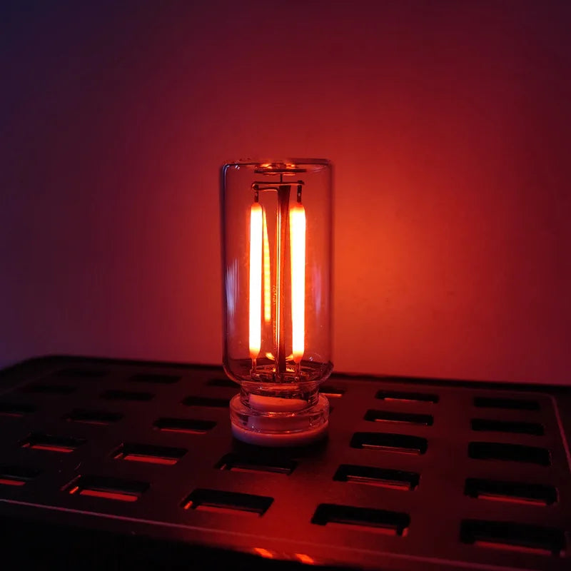 A glass light bulb with a warm filament glow sits on a metal tray.