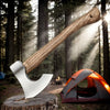 A hand-forged Viking tomahawk axe resting on a log next to an orange tent in a forest setting.