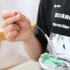 A hand is using a thin metal straw and a cleaning brush to clean a glass bottle.